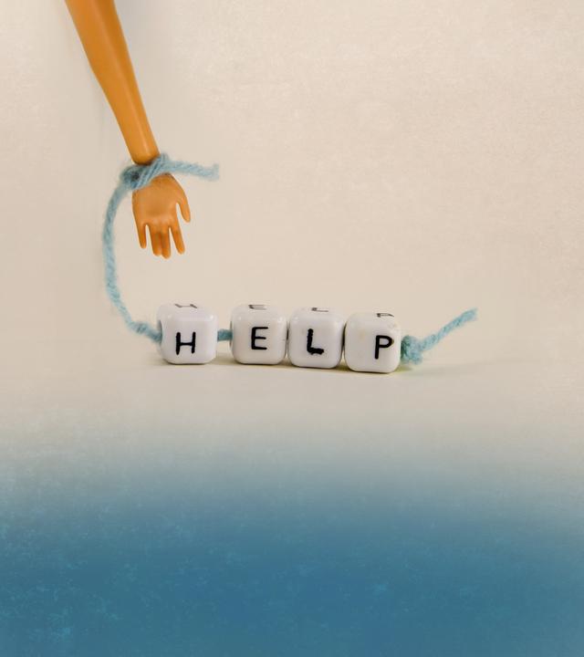 Kleine Hand hält ein Band mit Hölzkötzchen mit Aufschrift "Help"