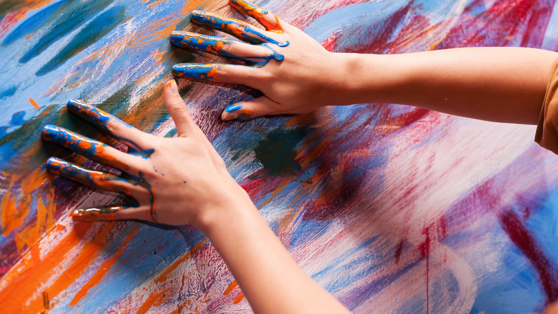 Hände mit Farbe malen auf einer bunten Leinwand