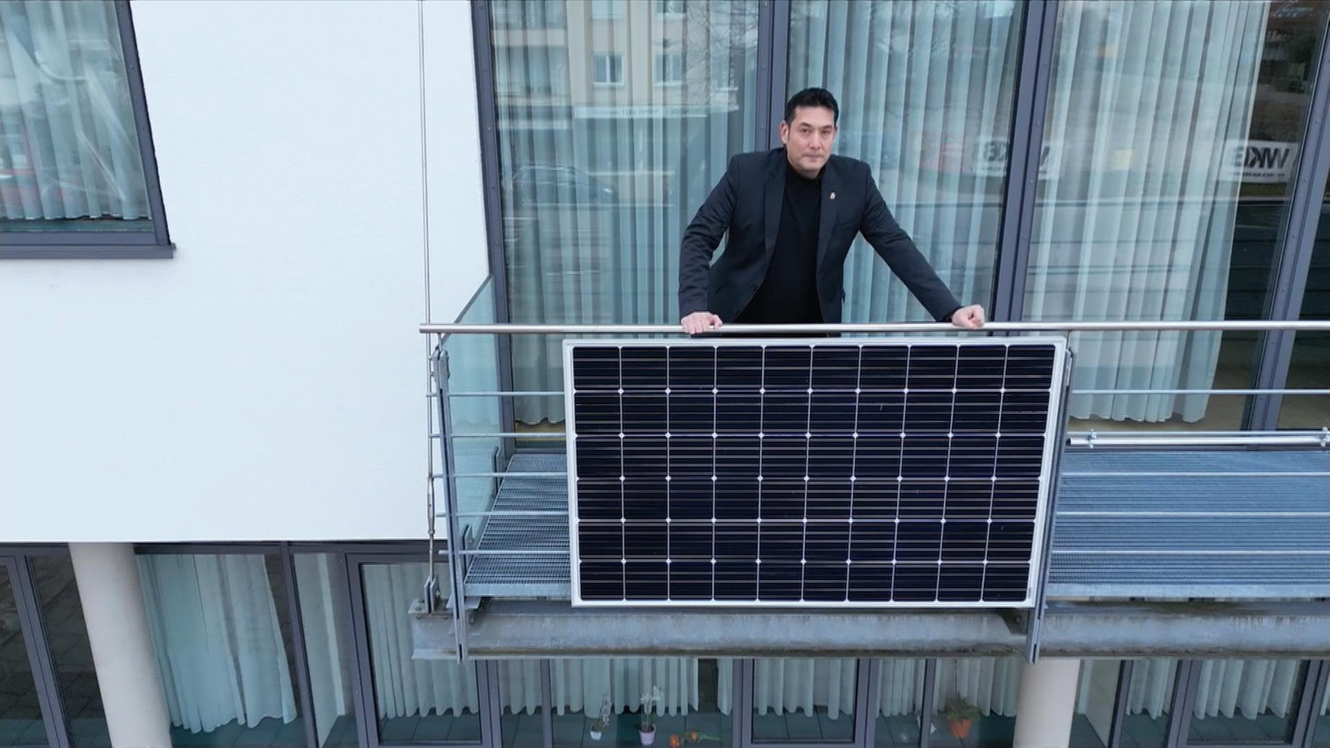 Mann steht auch Balkon mit einem Solarpanel.