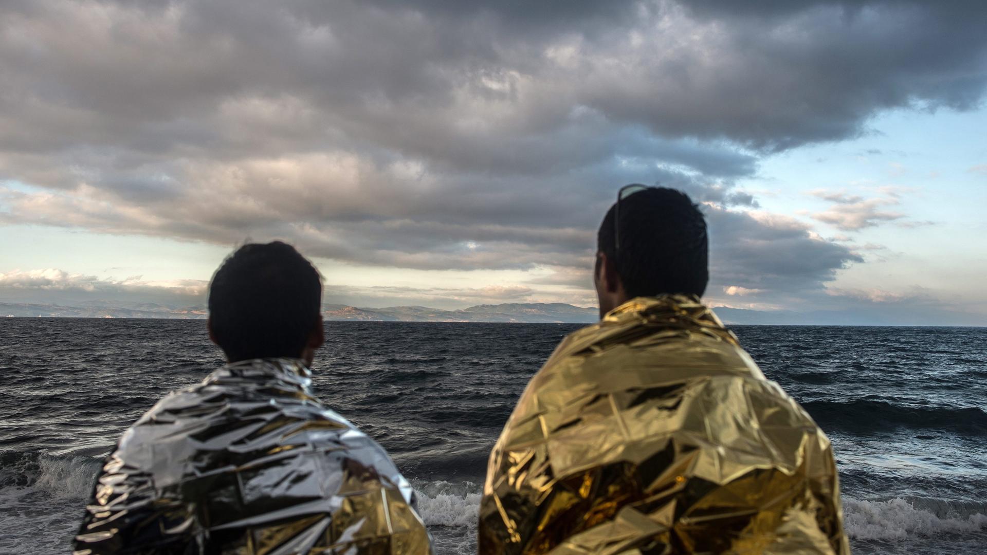 MIgranten sitzen auf einem Felschen und schauen aufs Meer