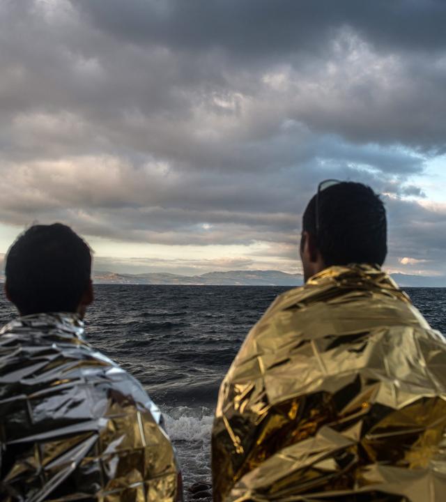 MIgranten sitzen auf einem Felschen und schauen aufs Meer