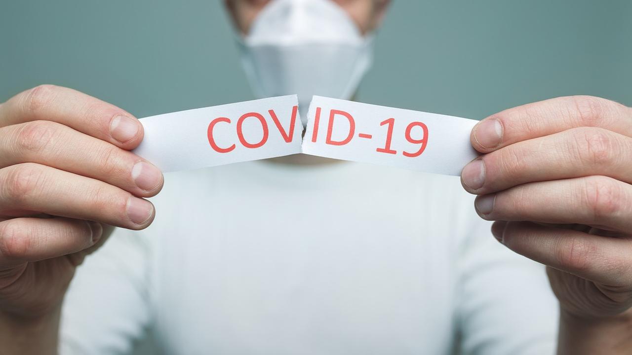 The man is holding a sheet that says "Covid-19" on it.