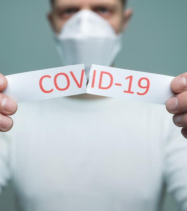 Mann hält Blatt mit der Aufschrift "Covid-19" hoch