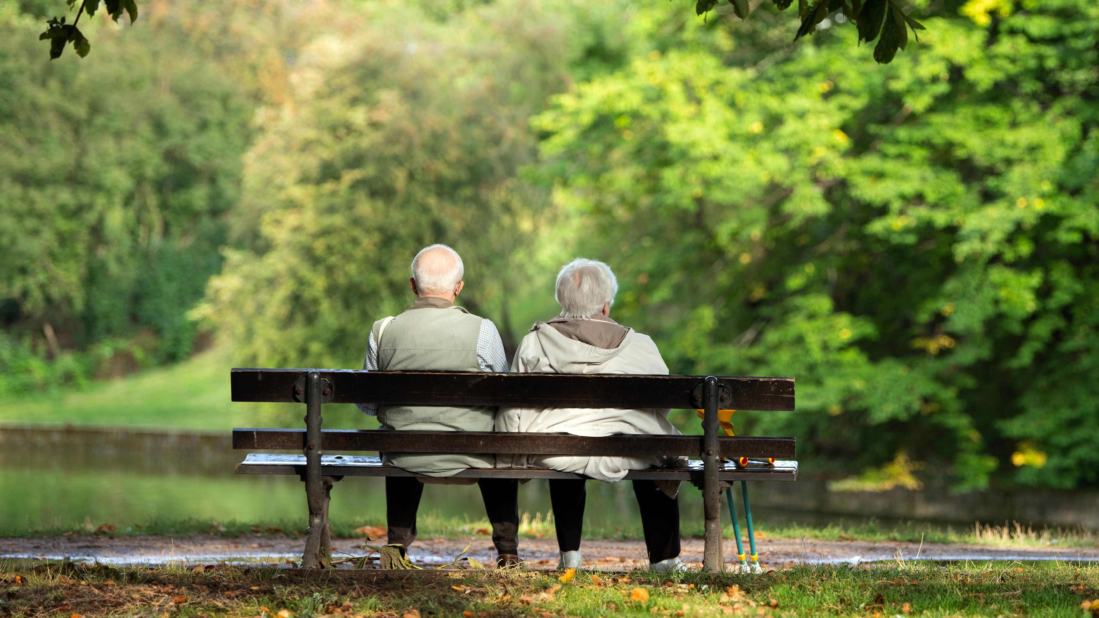 Zwei Rentner sitzen auf einer Bank und schauen ins Grüne