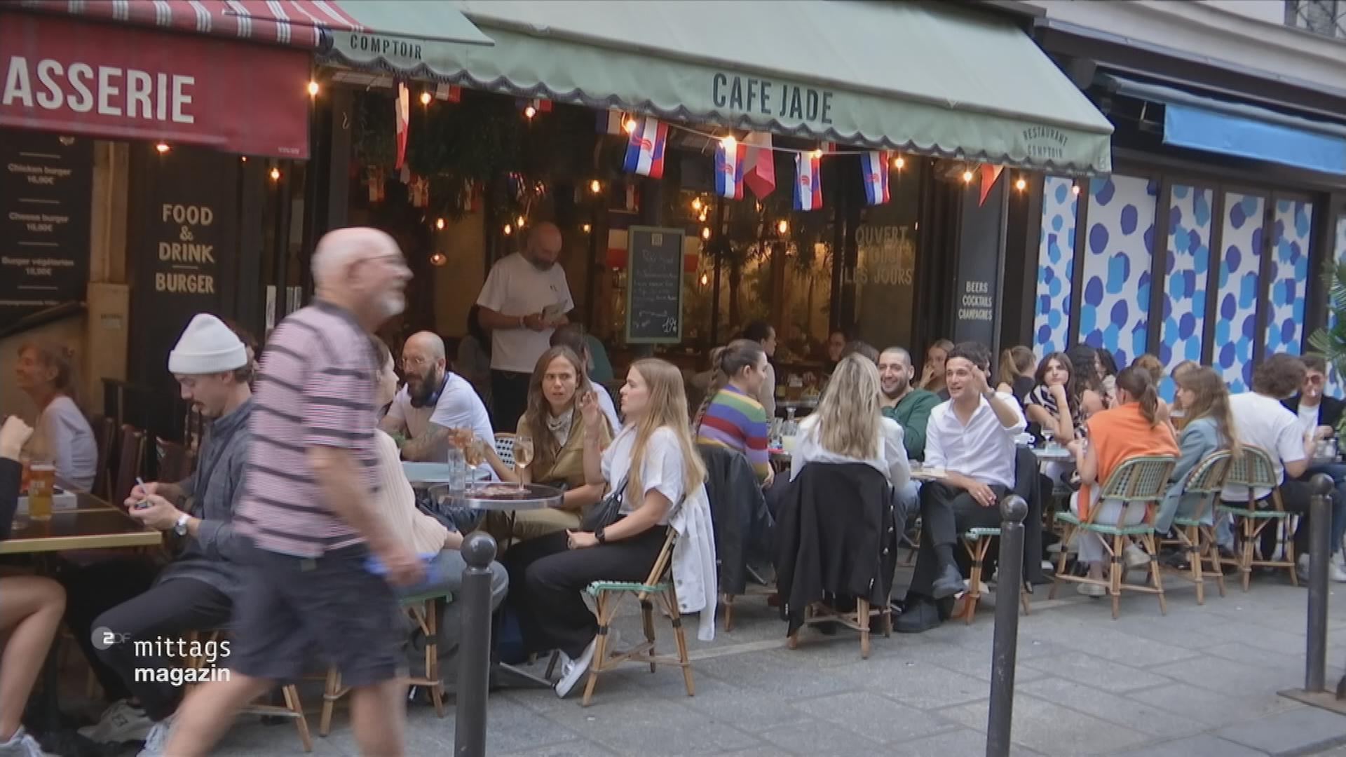 Menschen sitzen an Tischen vor einem Café in Paris