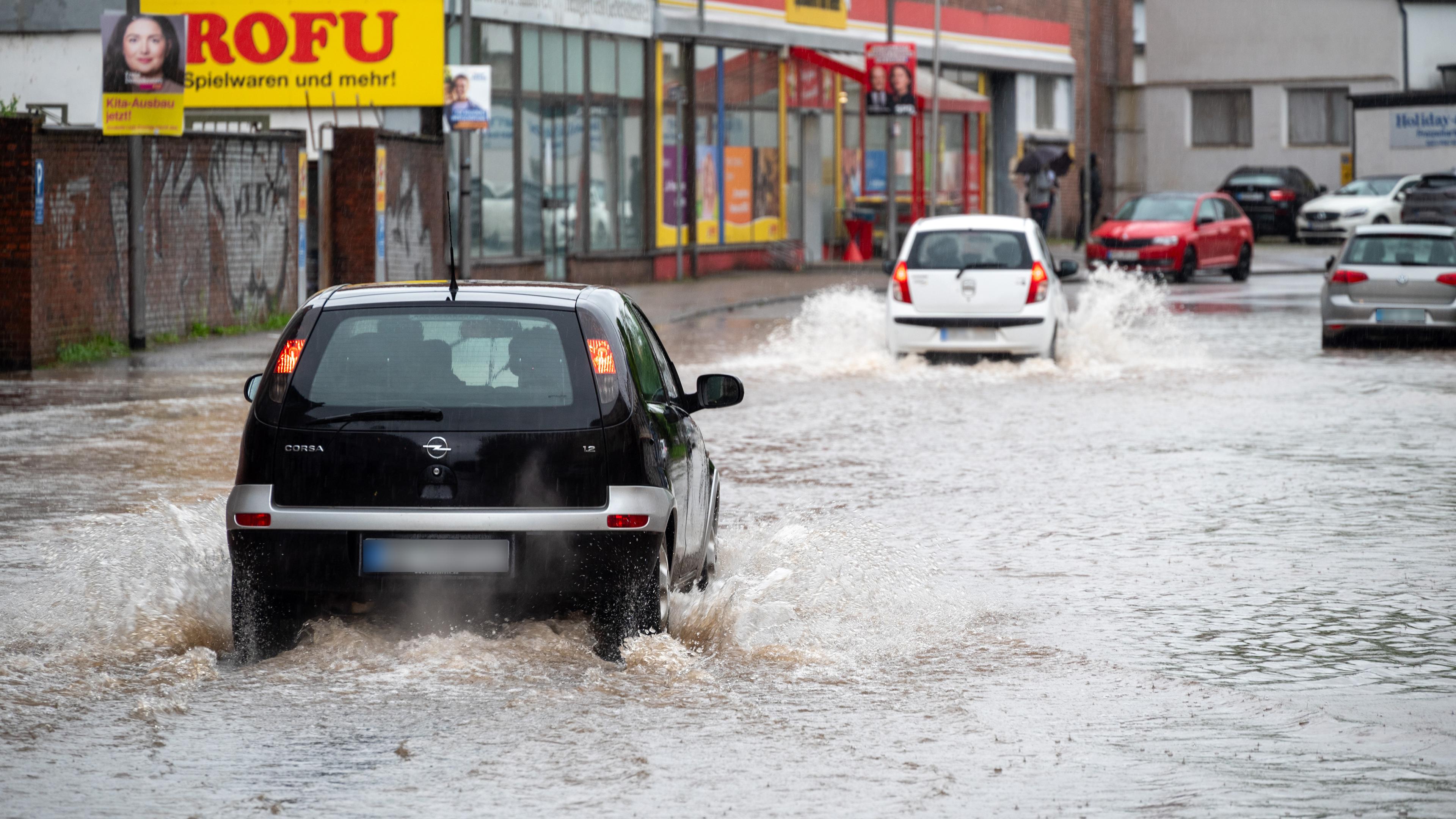 Autofahrer fahren trotz der Überschwemmungen in der Fischbachstrasse durch die steigenden Fluten.