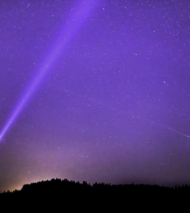 Mensch sucht mit einer Taschennlampe den Himmel nach außeriridschem Leben ab