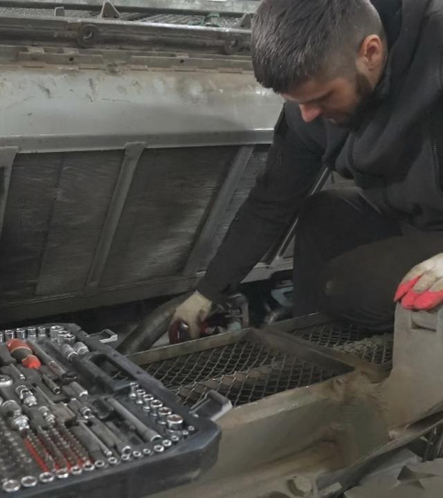 Ein Mann kniet auf dem Boden und repariert und wartet eine Maschine mit einem Werkzeugkasten.