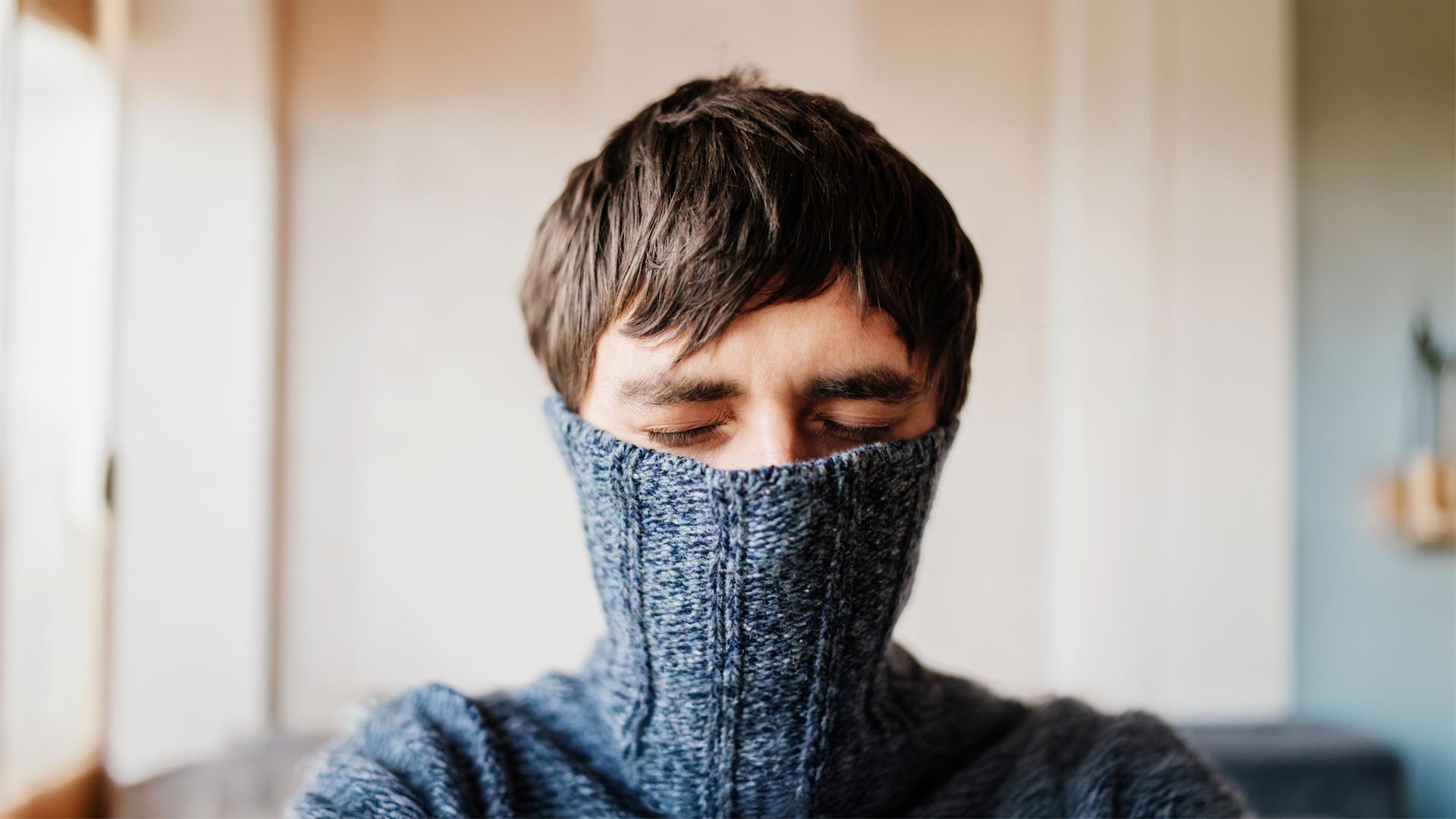 Mann mit geschlossenen Augen versteckt sein Gesicht in einem Pullover.