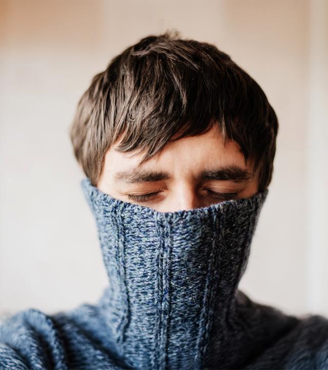 Mann mit geschlossenen Augen versteckt sein Gesicht in einem Pullover.