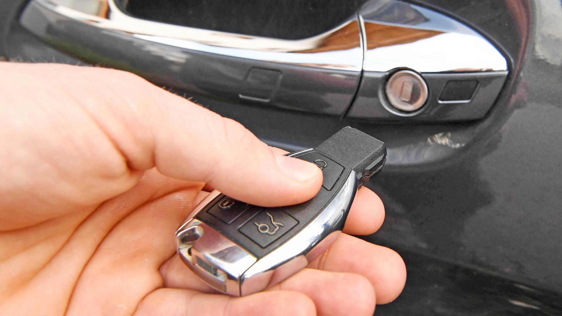 Hand mit Autoschlüssel, im Hintergrund ein Autotürgriff