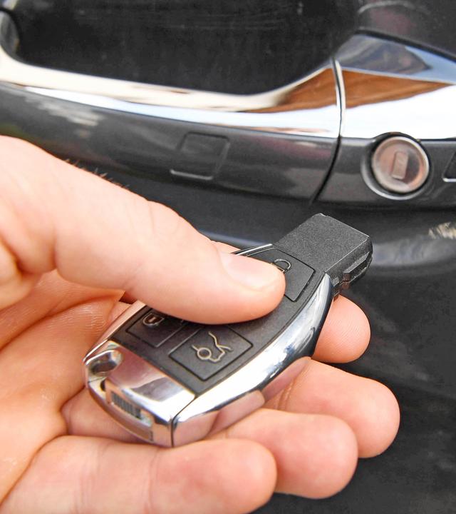 Hand mit Autoschlüssel, im Hintergrund ein Autotürgriff