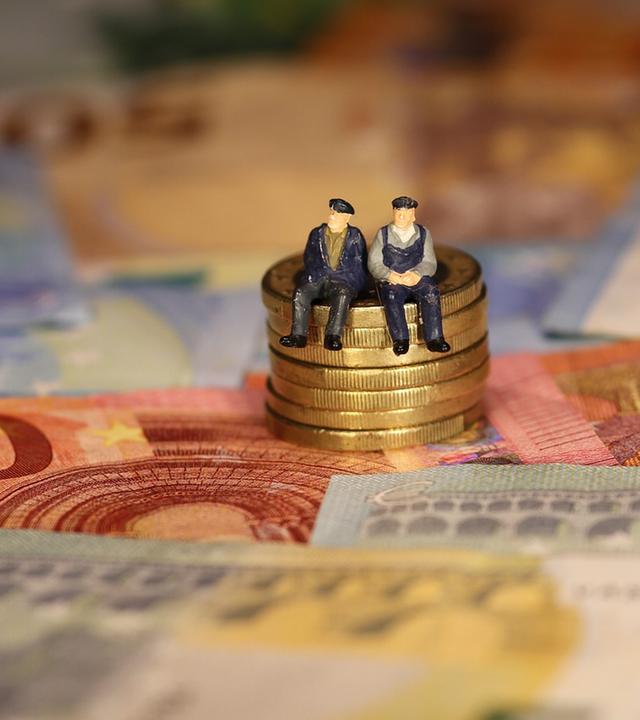 Puppen (Senioren) sitzen auf einem Stapel Münzen