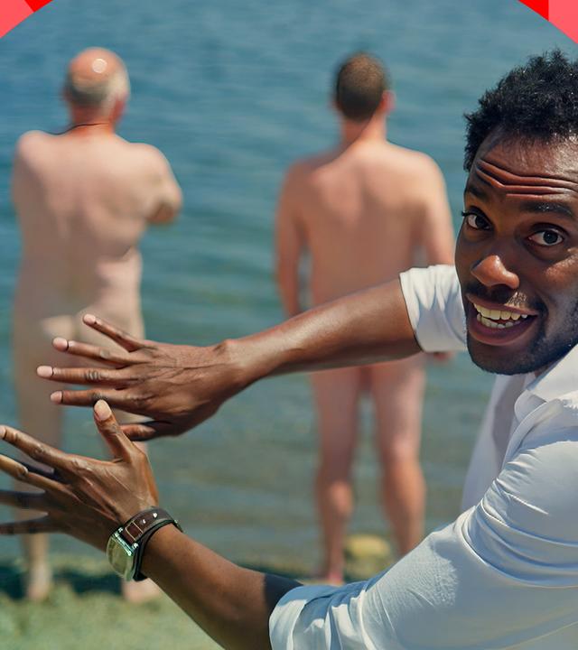 "Unser erstaunlicher Po": Host Anthony Morgan steht vor zwei nackten Männern, die mit dem Rücken zu ihm stehen. Er deutet mit seinen Händen die Geste an, ihre Hintern zu bedecken