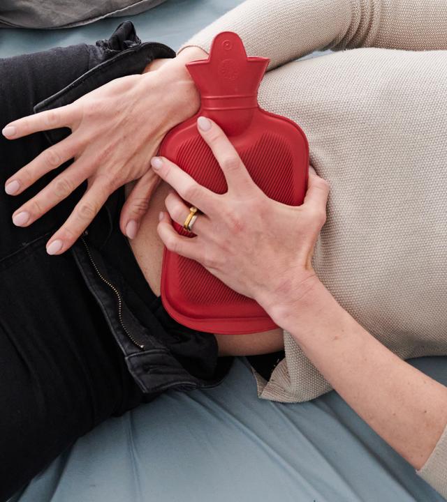 Frau hält sich eine Wämflasche auf den Bauch