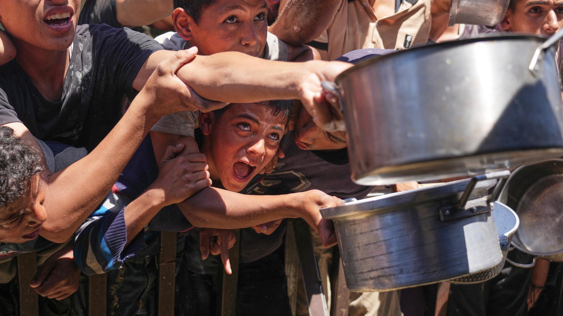 Palestinians struggle to receive cooked food distributed at a community kitchen in the Muwasi area of Khan Younis, in the Gaza Strip, Friday, May 23, 2025.