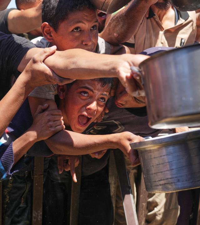 Palestinians struggle to receive cooked food distributed at a community kitchen in the Muwasi area of Khan Younis, in the Gaza Strip, Friday, May 23, 2025.