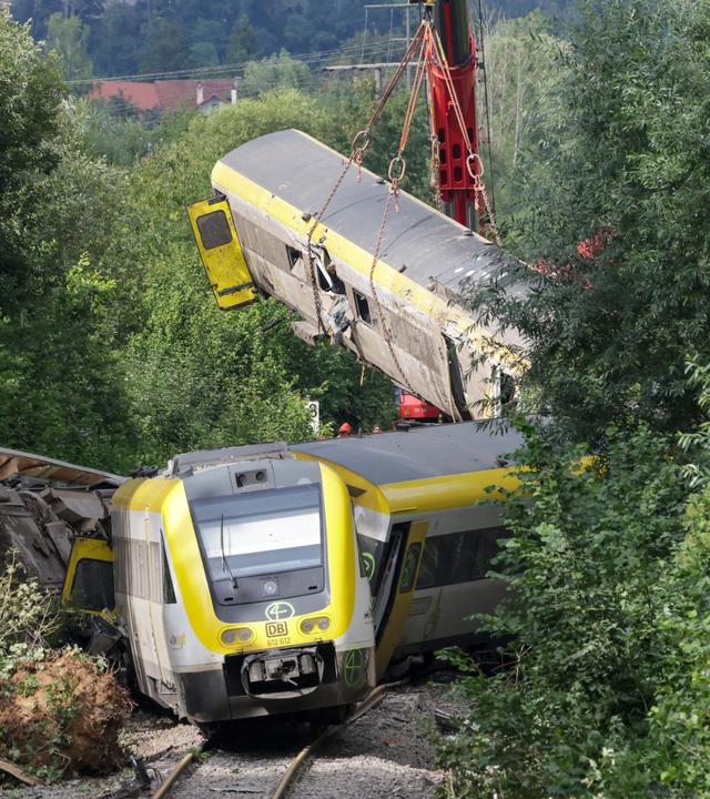 28.07.2025, Baden-Württemberg, Riedlingen: Mit einem Kran wird an der Unfallstelle, an der ein Regionalzug entgleist ist, ein Waggon angehoben.
