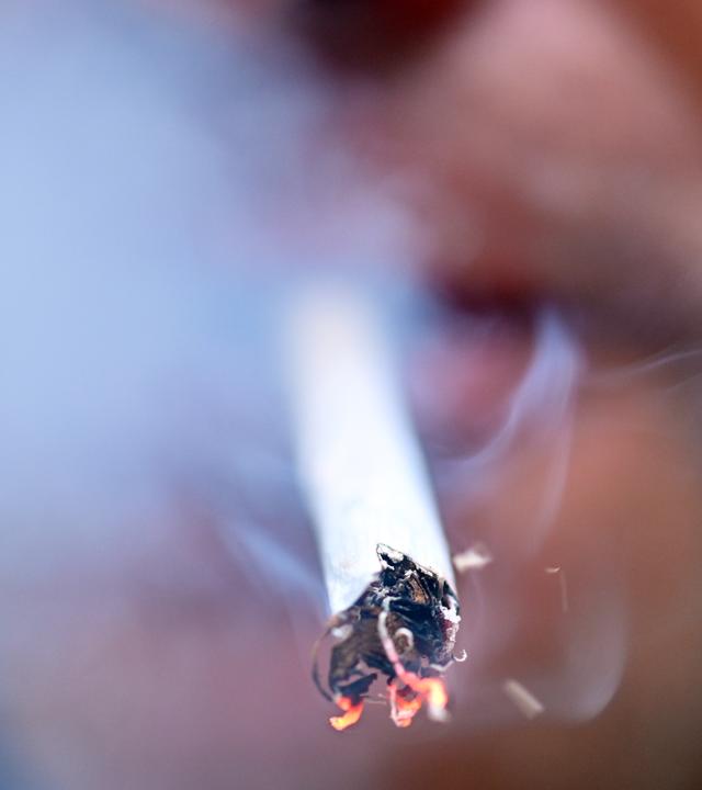 Person raucht eine glühende Zigarette