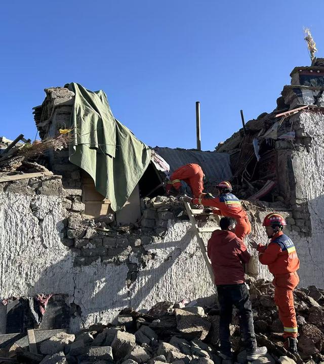 Es sind Rettungskräfte zu sehen, welche vor einen betroffenen zerstörten Haus stehen.