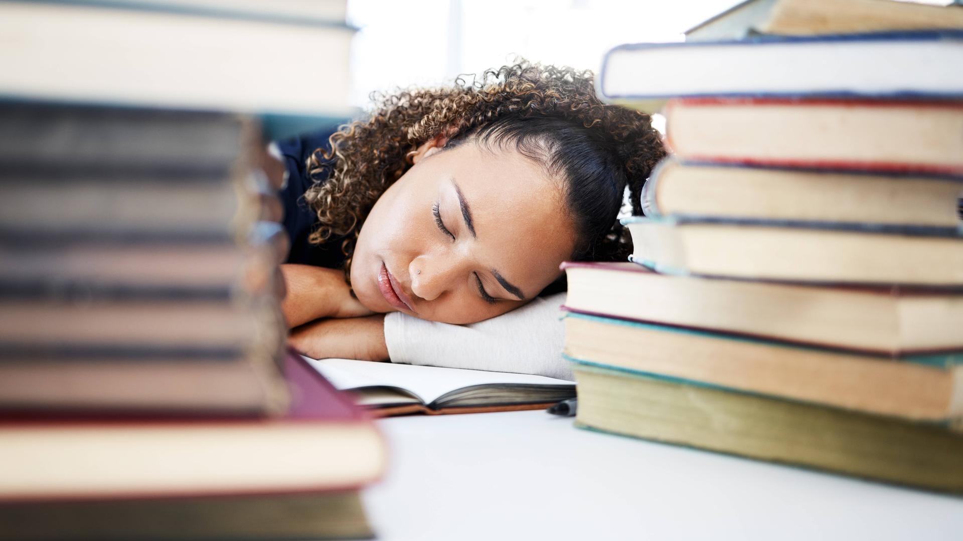 Müde Schülerin schläft zwischen Büchern in der Schule