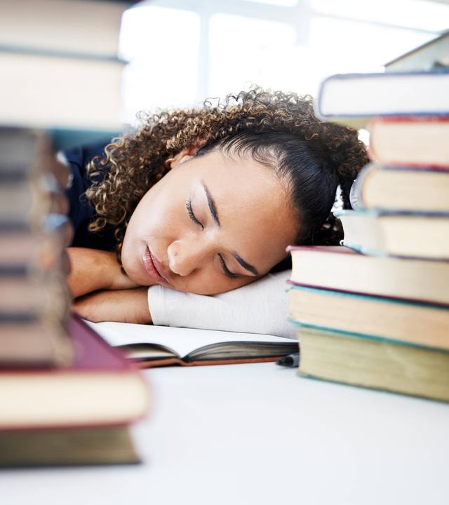 Müde Schülerin schläft zwischen Büchern in der Schule