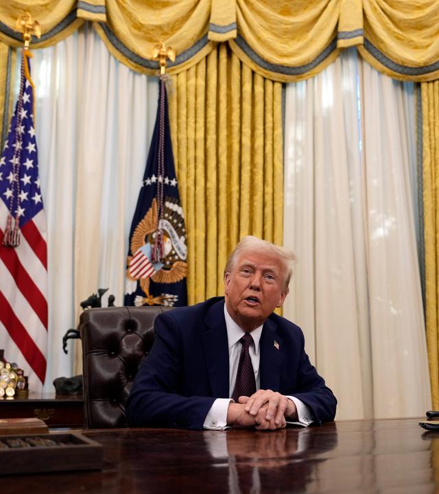 Trump sitz am Schreibtisch, Fahnen im Hintergrund