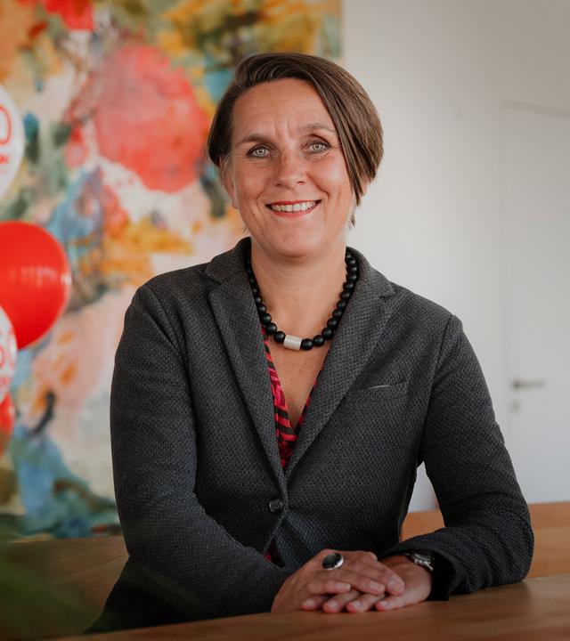 "einfach Mensch - Jubiläum: Die "Aktion Mensch" wird 60 Jahre! (2)": Christina Marx, Sprecherin der "Aktion Mensch" sitzt an einem Tisch und lächelt in die Kamera.