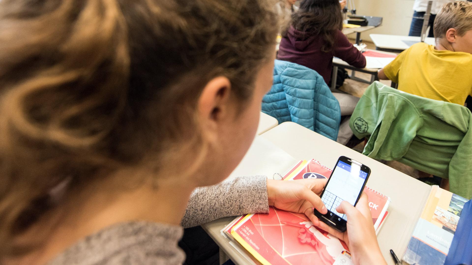Mädchen schaut während des Unterrichts auf ihr Handy