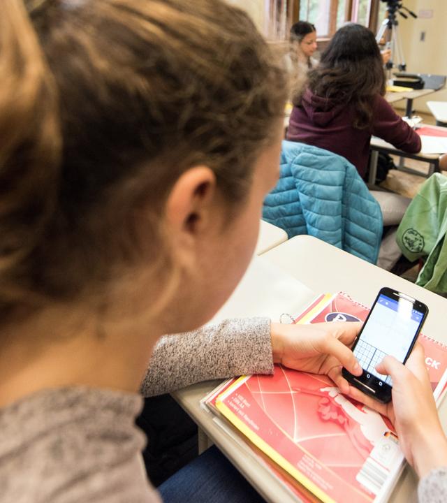 Mädchen schaut während des Unterrichts auf ihr Handy