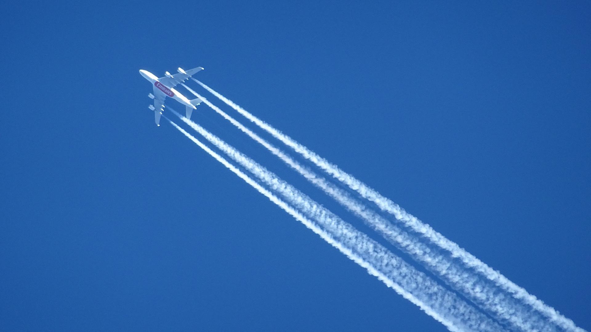 Ein Verkehrsflugzeug zieht einen langen Kondensstreifen am klaren Himmel hinter sich her - Symbol für die klimaschädlichen Auswirkungen des Luftverkehrs