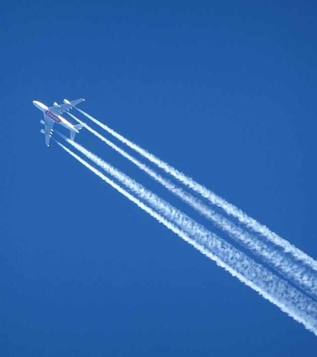 Ein Verkehrsflugzeug zieht einen langen Kondensstreifen am klaren Himmel hinter sich her - Symbol für die klimaschädlichen Auswirkungen des Luftverkehrs