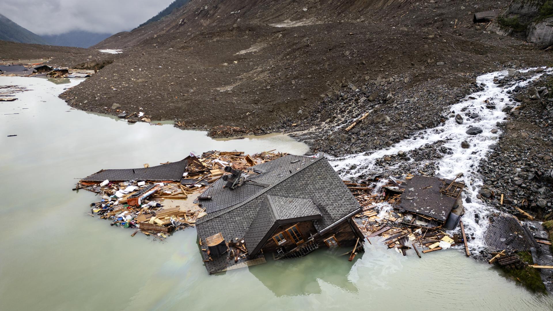 Ein teilweise verschüttetes Haus ragt aus Geröll und WasserTeilweise verschüttetes Haus ragt aus Geröll und Wasser – letzter sichtbarer Rest nach dem Gletschersturz in Blatten.