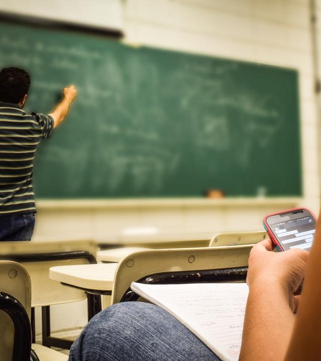 Ein Lehrer erklärt an der Tafel, während ein Schüler neben ihm ein Smartphone nutzt – Symbolbild für den digitalen Wandel und die Herausforderung, KI-Technologie sinnvoll im Unterricht einzusetzen.