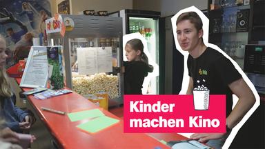 Kinder, die hinter Kinotheke stehen und Popcorn und Tickets verkaufen - darauf Schrift "Kinder machen Kino"