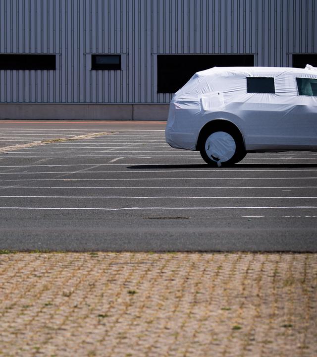 Ein einzelnes in Plane verpacktes Neufahrzeug steht auf einem Parkplatz. 