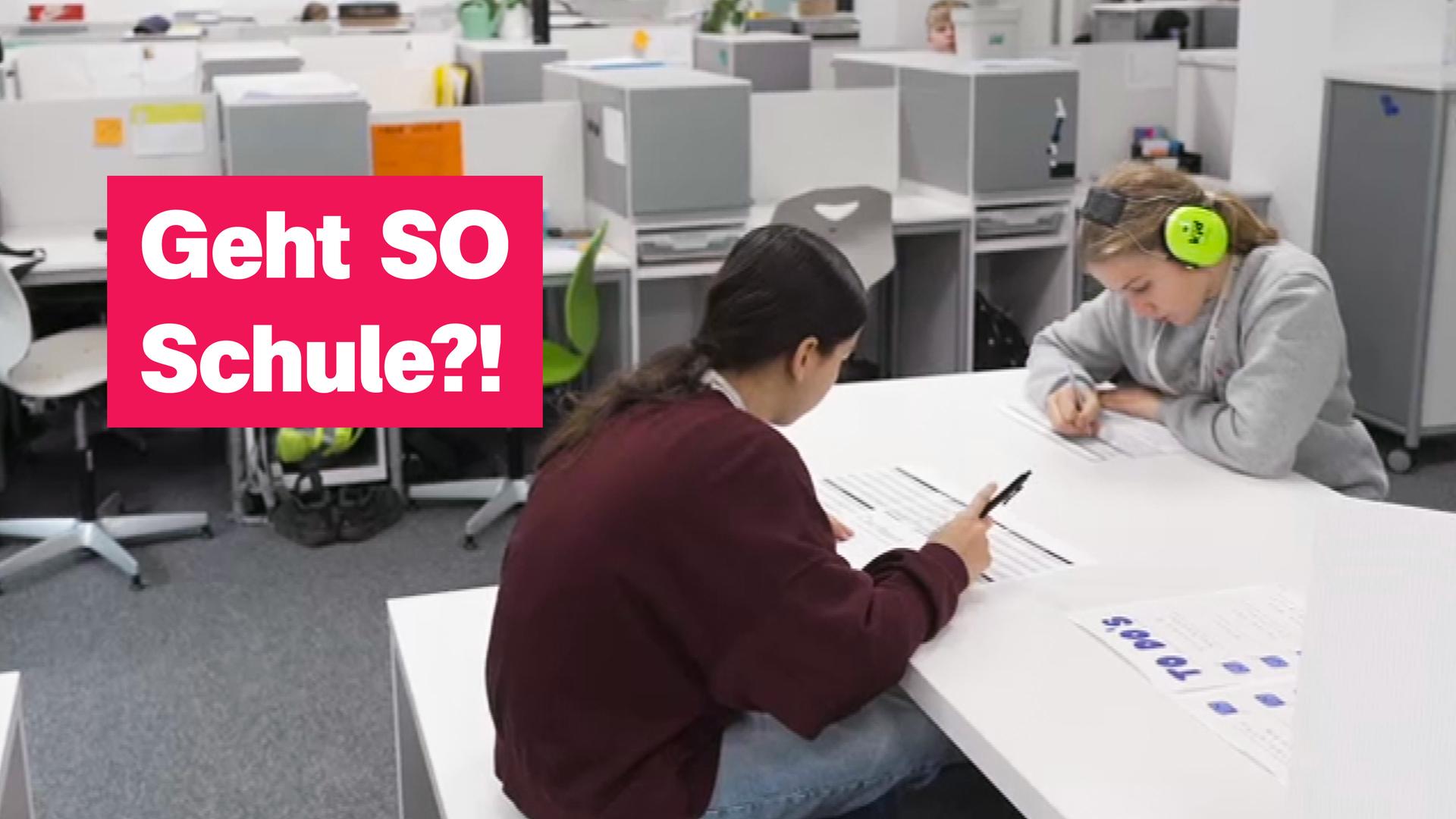 Auf dem Foto sind zwei Schülerinnen zu sehen, die an einem Gruppentisch gemeinsam lernen. Eine von ihnen trägt Lärmschutzkopfhörer in neongrün.