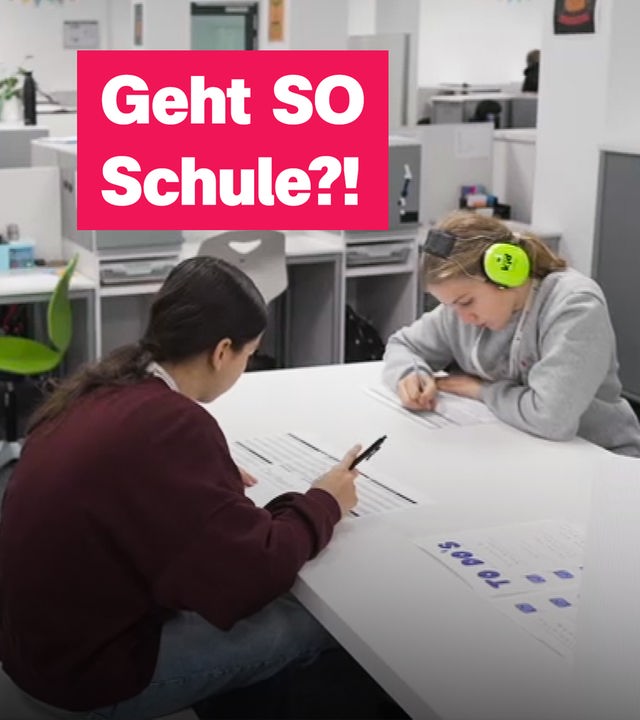 Auf dem Foto sind zwei Schülerinnen zu sehen, die an einem Gruppentisch gemeinsam lernen. Eine von ihnen trägt Lärmschutzkopfhörer in neongrün.