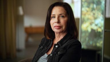 Manuela Freitag im Portrait fotografiert. Sie sitzt mit dem Gesicht der Kamera zugewandt und schaut ernst. Manuela Freitag ist 64 Jahre alt und trägt ihre dunkelbraunen Haare schulterlang. 