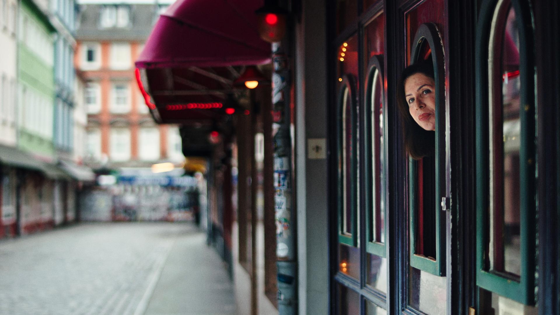Zu sehen ist die leere Herbertstraße. Auf der rechten Seite des Bildes kann man die Separees der Prostituierten erkennen. Aus einem der Fenster streckt Manuela Freitag ihren Kopf und blickt auf die Straße.