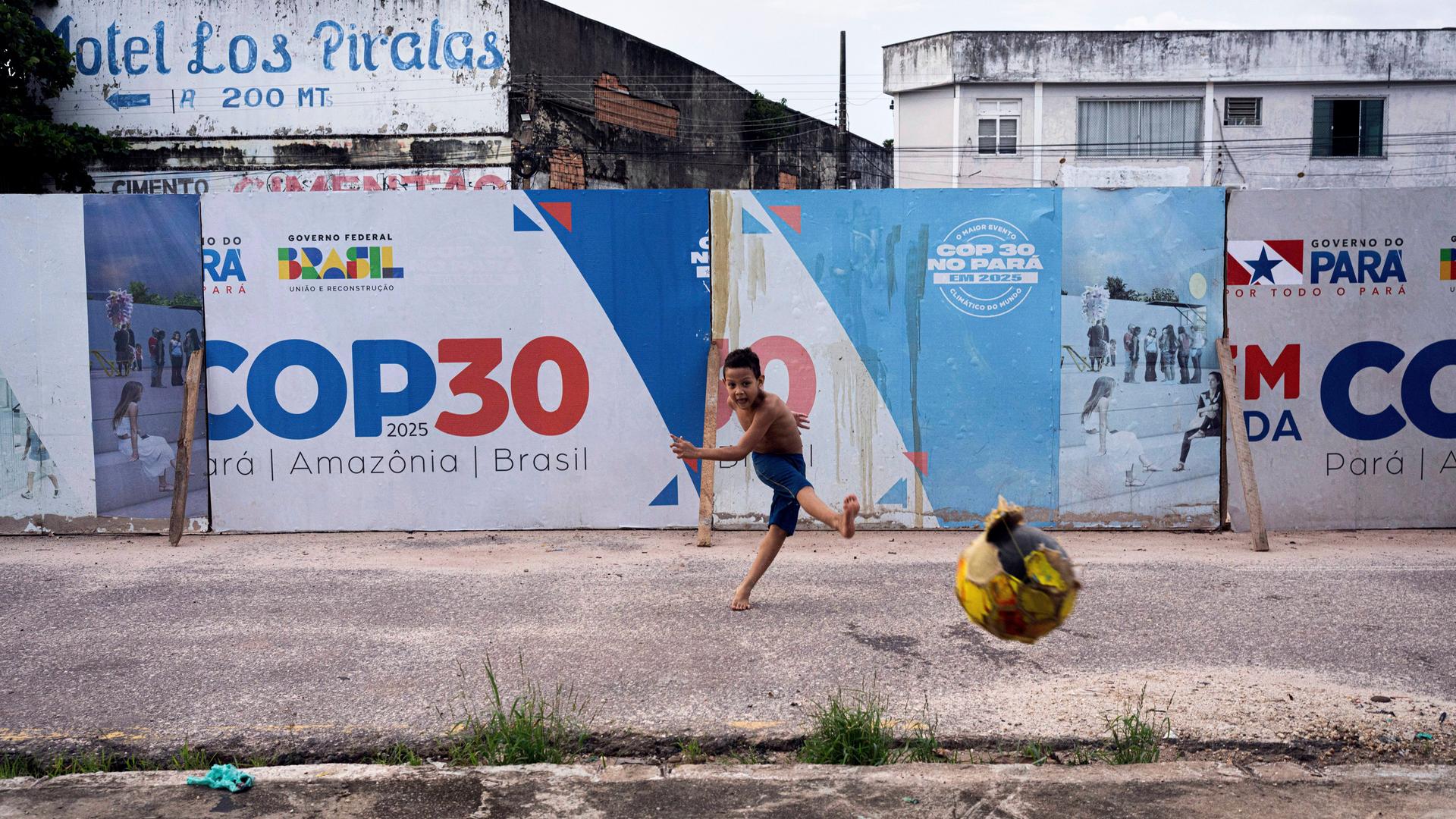 Junge spielt Ball vor COP30-Schild