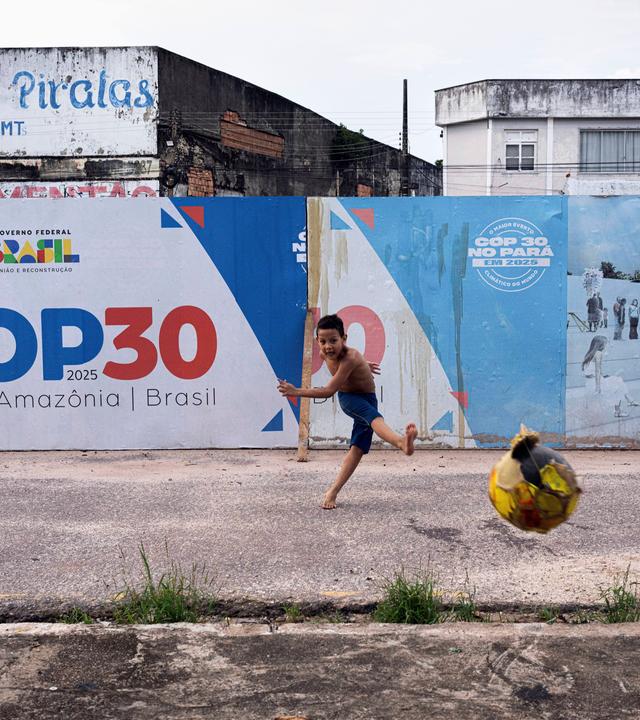 Junge spielt Ball vor COP30-Schild