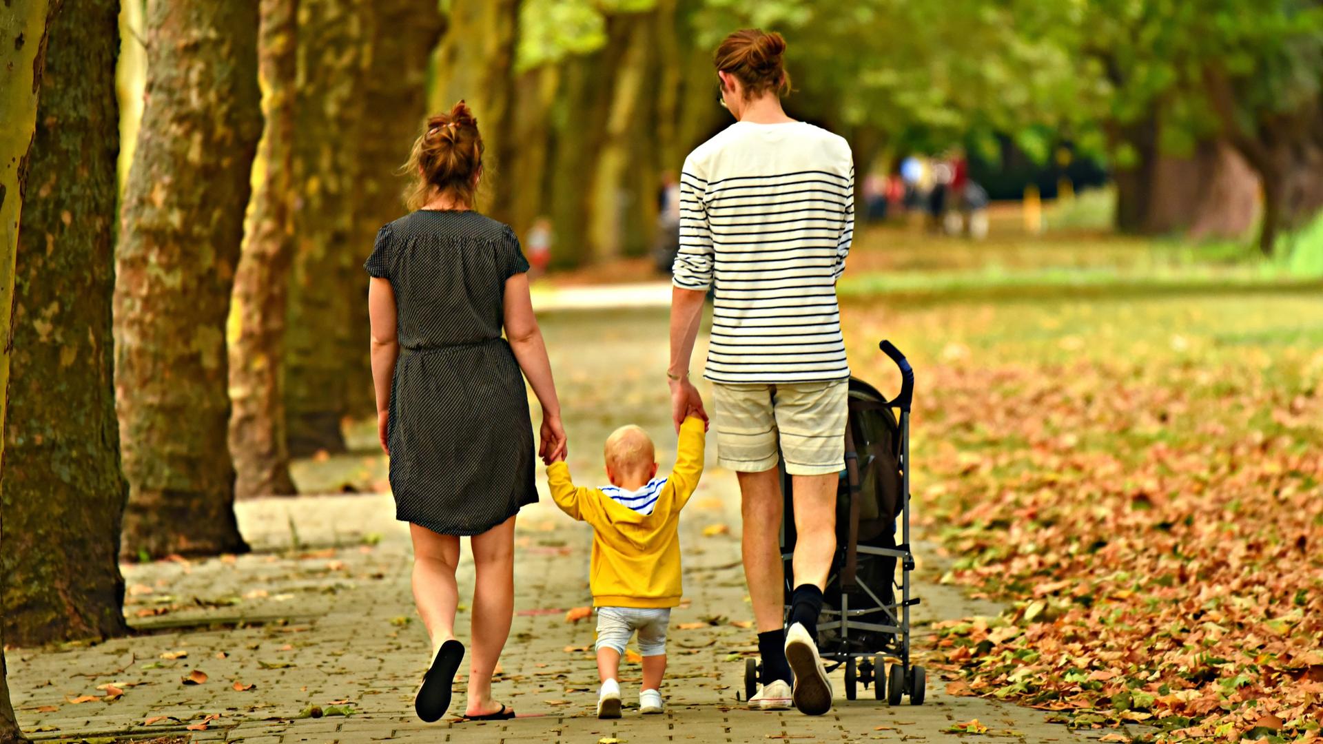 Begleitete Elternschaft: Eltern mit Unterstützungsbedarf können ihre Kinder mit professioneller Hilfe selbstständig erziehen. Das Bild zeigt zwei Erwachsene mit einem Kind in der Mitte bei einem Herbstspaziergang.