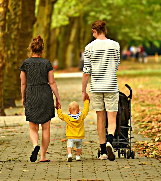 Begleitete Elternschaft: Eltern mit Unterstützungsbedarf können ihre Kinder mit professioneller Hilfe selbstständig erziehen. Das Bild zeigt zwei Erwachsene mit einem Kind in der Mitte bei einem Herbstspaziergang.