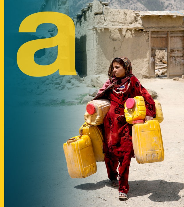 Eine Frau mit rotem Gewand trägt leere Wasserkanister durch eine sandige Landschaft. 