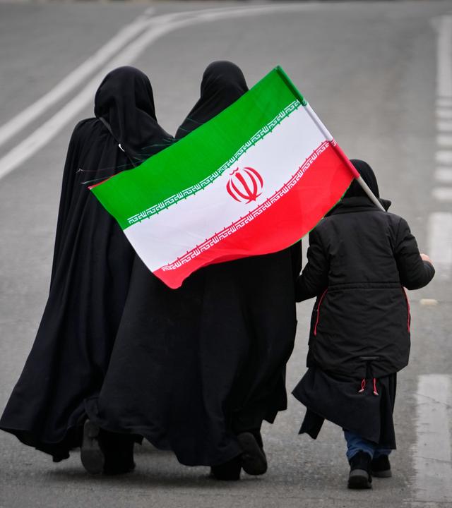 20.03.2026, Iran, Teheran: Zwei Frauen und ein Kind, die eine iranische Flagge halten, gehen zum Freitagsgebet zur Großen Moschee Imam Khomeini in der iranischen Hauptstadt.