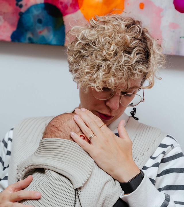 "37°Leben: Das Wochenbett - Glückshormone und Albträume": Jacqui trägt ihren Sohn Sohn Jonah im Tragetuch vor sich und schaut ihn an.