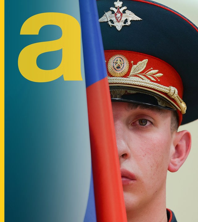 Ein russischer Soldat mit Soldatenhut. Sein Gesicht wird zur Hälfte von einer russischen Flagge verdeckt.