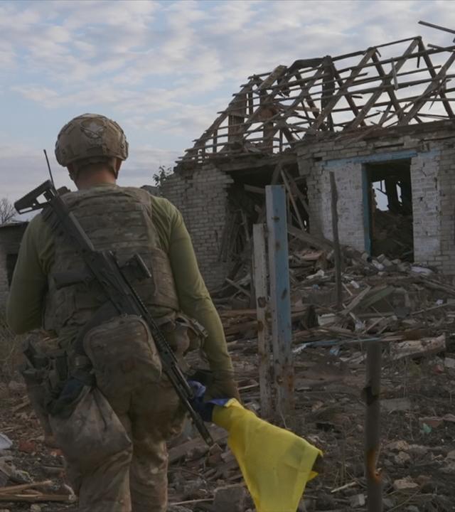 Ukrainischer Soldat läuft auf zerstörtes Haus zu.