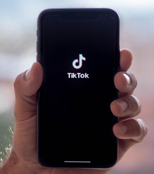 Die Jagd nach Klicks auf TikTok: Warum der Ton im Parlament rauer wird (Bild: Eine Hand hält ein Smartphone, auf dessen Display TikTok geöffent ist)
